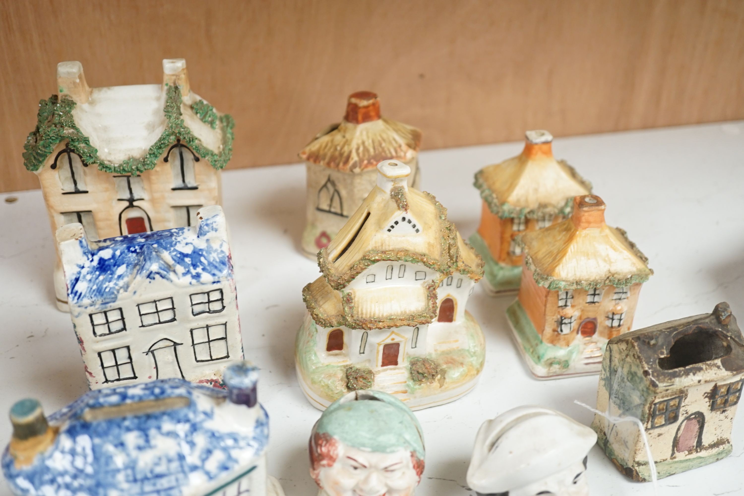 Twelve Staffordshire pottery money boxes, three with sponged decoration, modelled as cottages or heads, tallest 13.5 cms high.